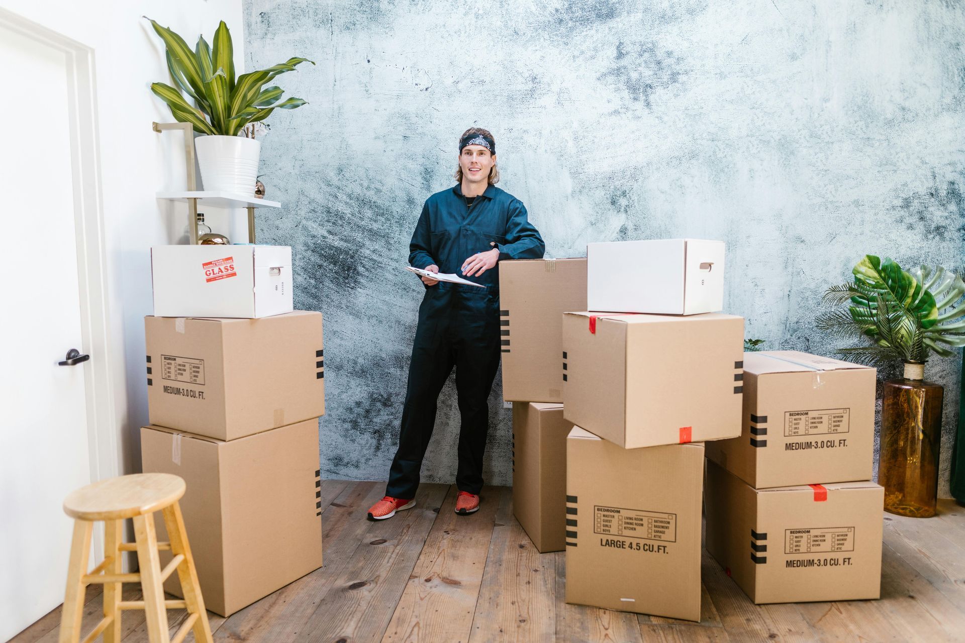 Woman in work uniform stands by moving boxes in a room.