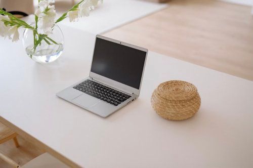 a Laptop Computer is Sitting on a White Table Next to a Vase of Flowers  — The Home Assembly In Avoca Beach, NSW