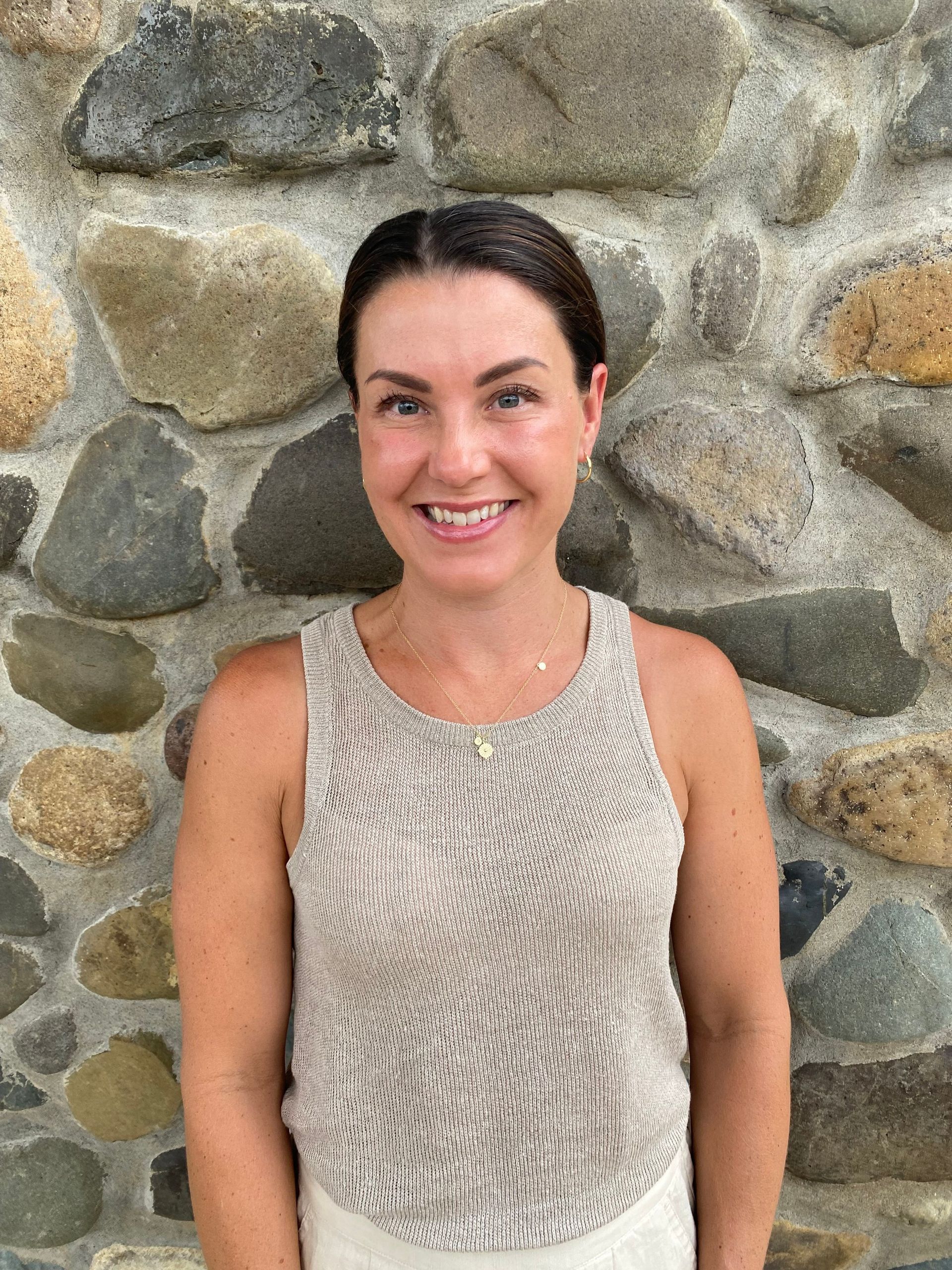 A Woman in A Tank Top Is Smiling in Front of A Stone Wall — The Home Assembly In Avoca Beach, NSW