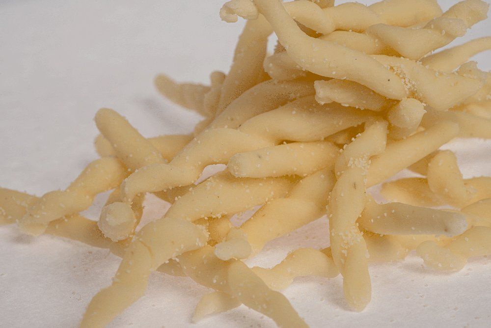 Primo piano di fettuccine crude, di colore giallo chiaro, disposte su una superficie bianca.