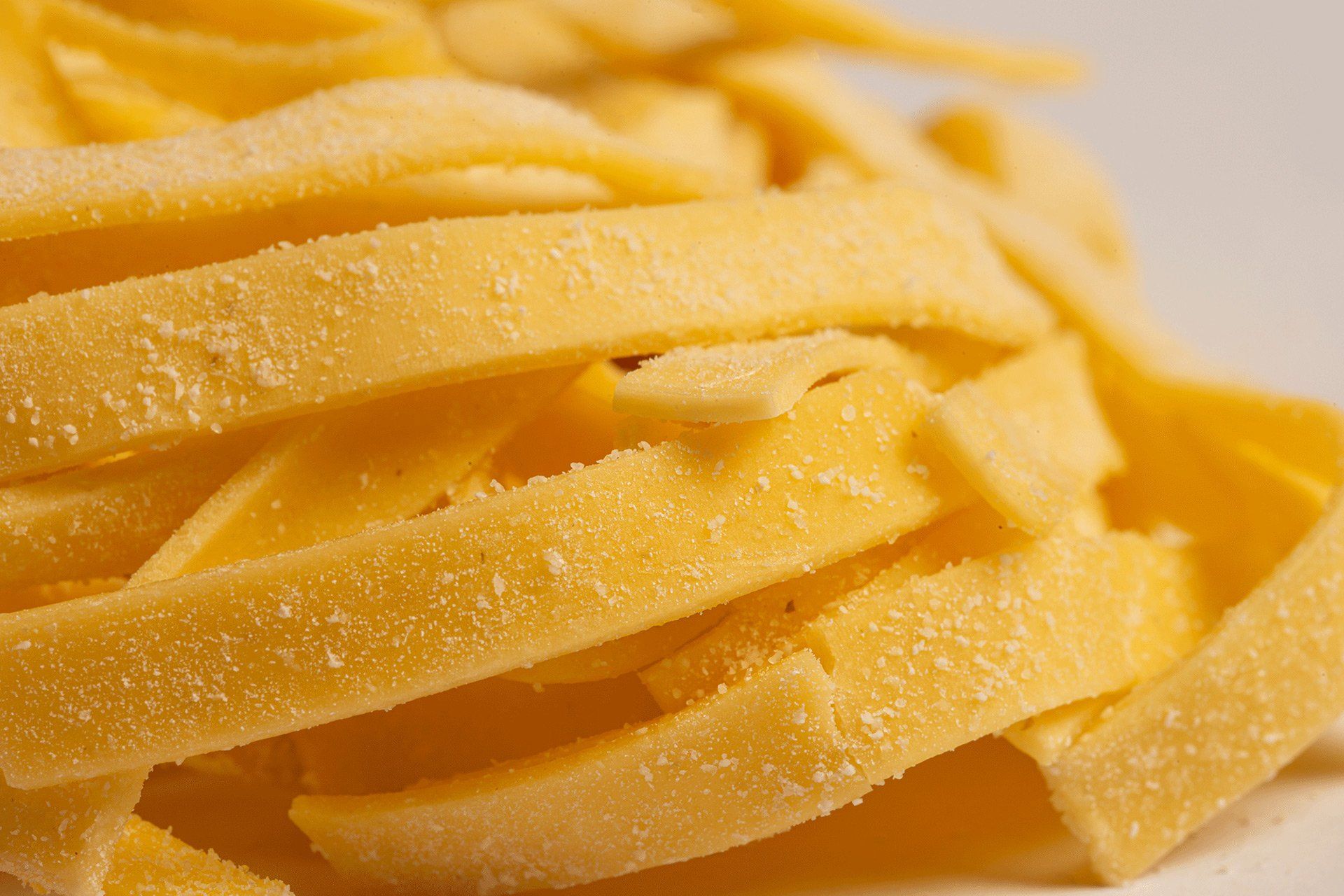 Primo piano di fettuccine fresche gialle, leggermente infarinate.