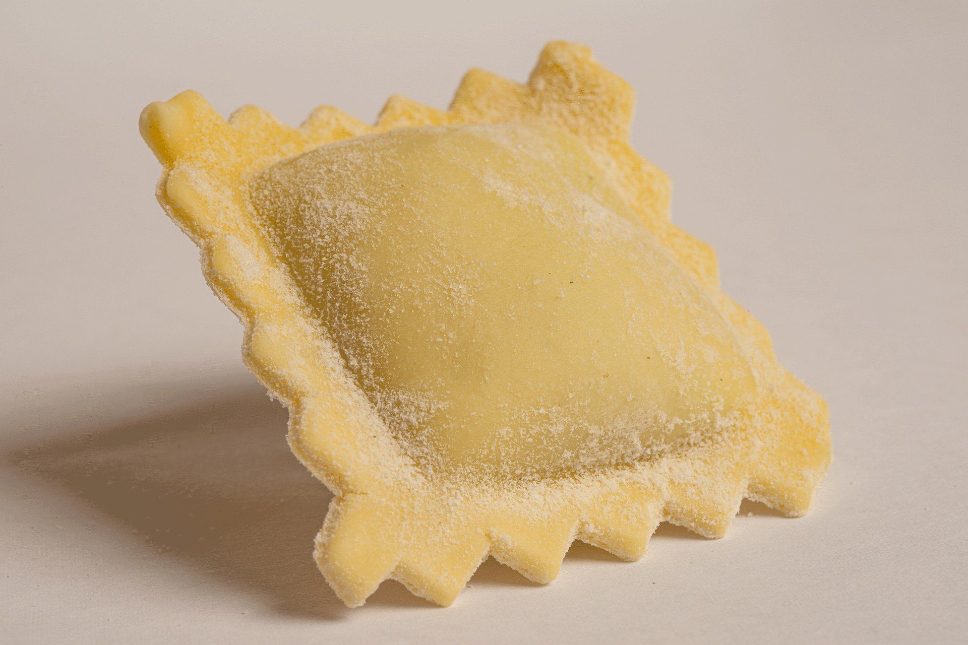 Ravioli singoli, di forma quadrata, con bordi smerlati, di colore giallo chiaro, isolati su fondo bianco.