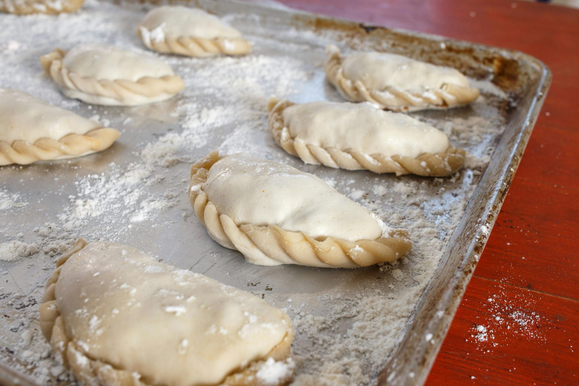 Empanadas su una teglia, spolverate di farina, pronte per la cottura.