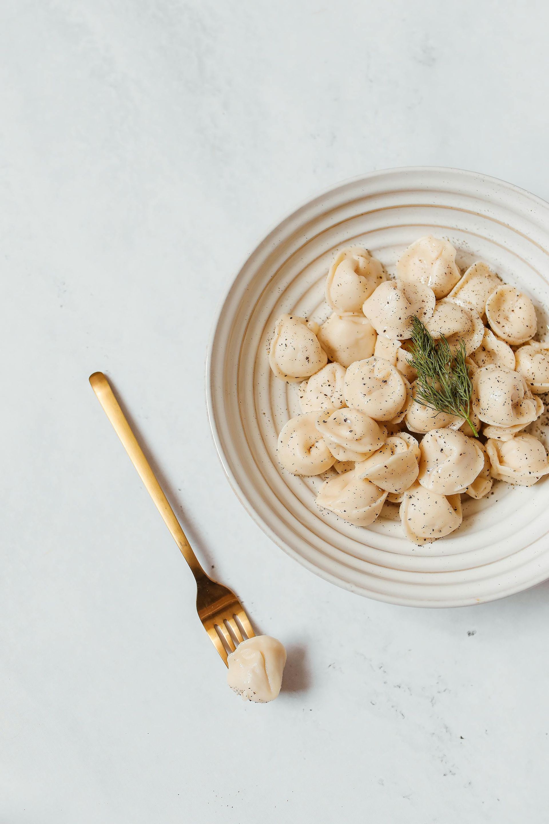 Pasta al pesto in una ciotola, forchetta dorata, vista dall'alto.