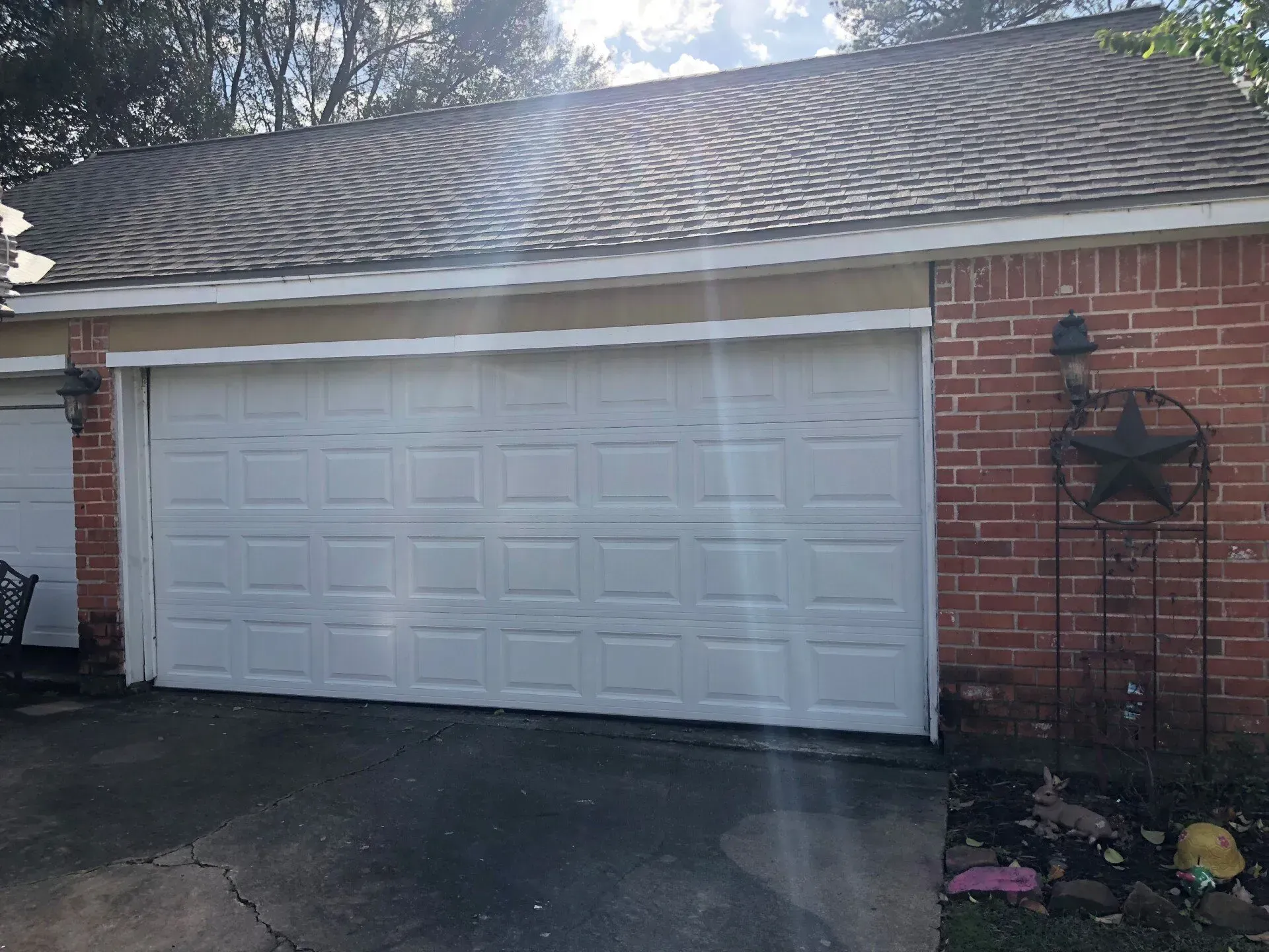 A white two-car garage door attached to a red brick house with an asphalt roof and a metal star wall decoration.