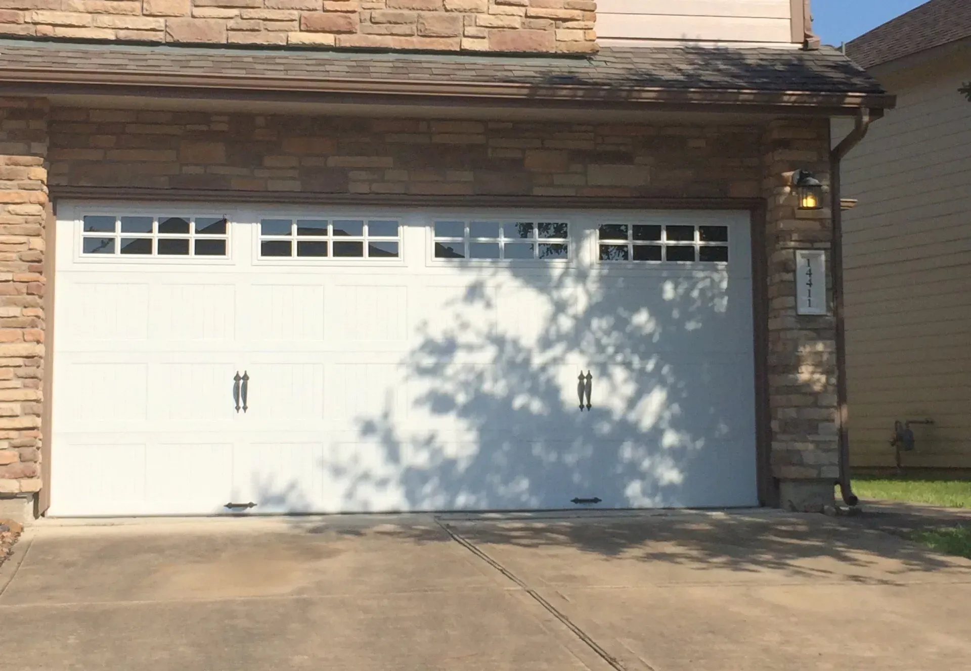 A white residential garage door with four windows and decorative hardware, framed by stone siding.
