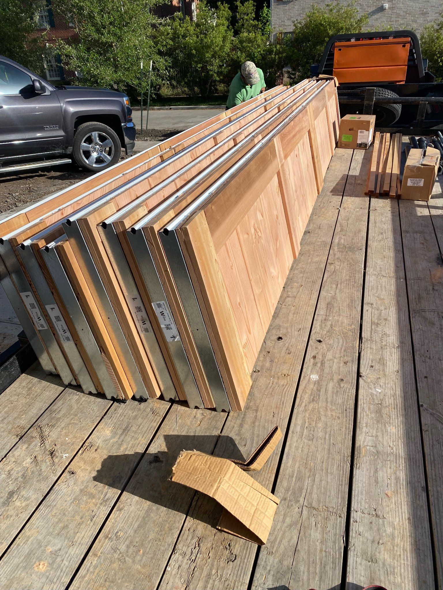 A flatbed trailer parked outdoors carrying a stack of long, narrow construction panels with wood-grain surfaces.