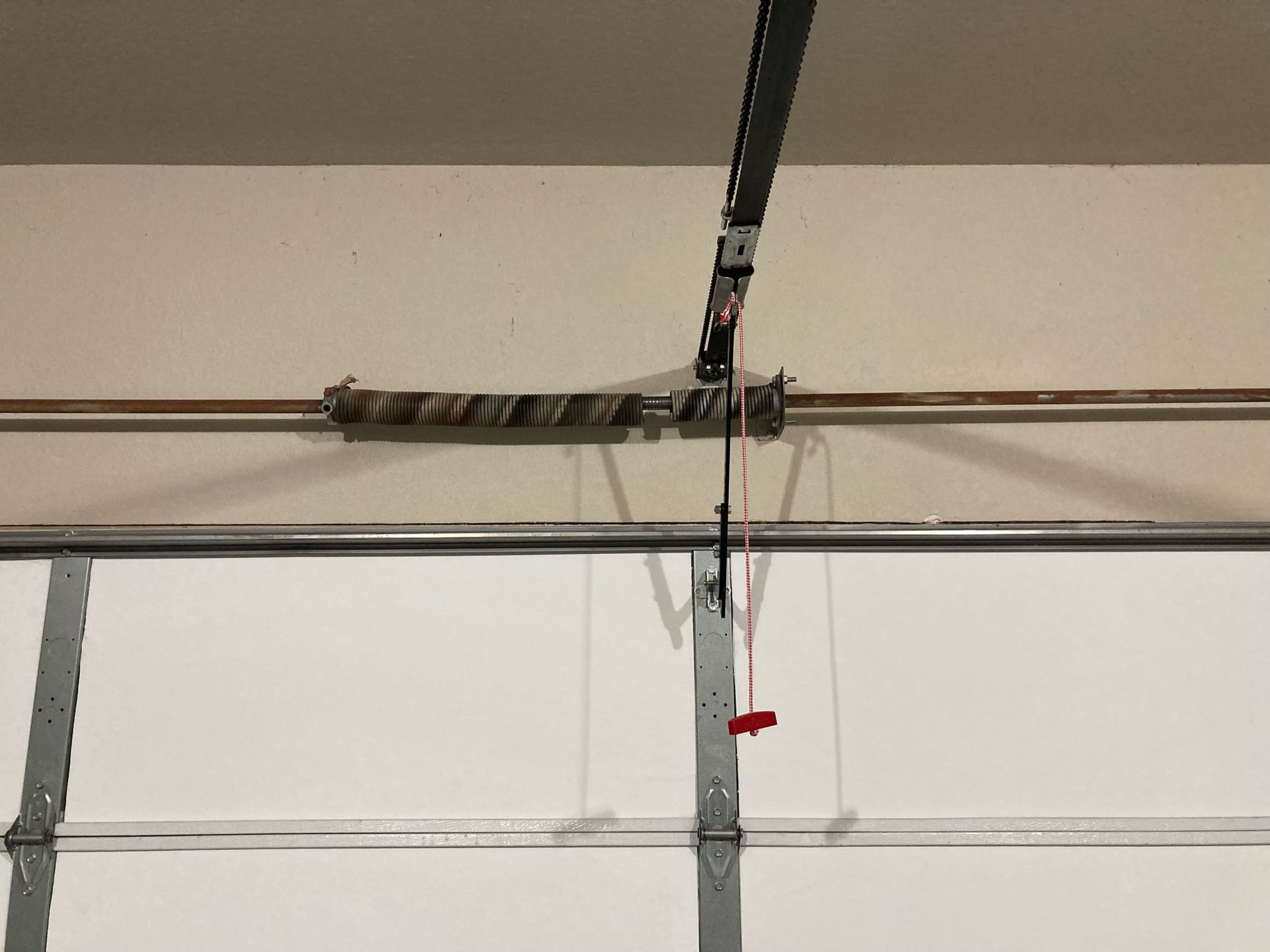 A metal torsion spring mounted on a garage door shaft with a red emergency release handle hanging below.