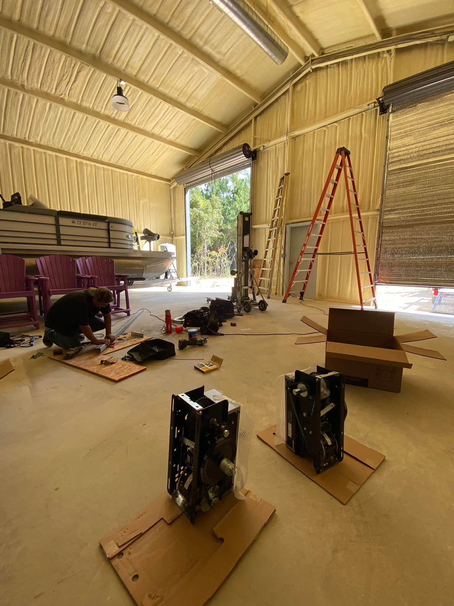 A person works in a large, unfinished workshop with two black industrial engines on cardboard floor mats.