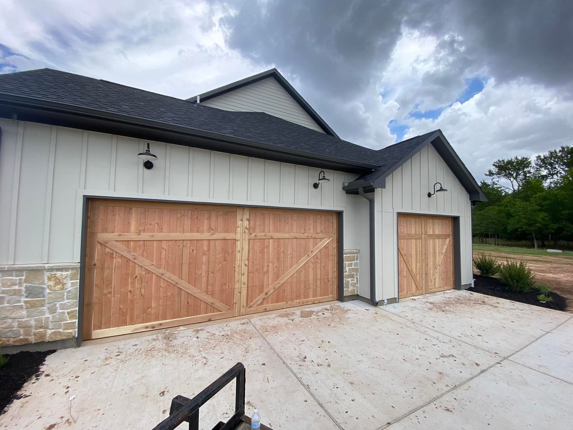 Modern exterior of a house with a three-car garage featuring light wood carriage-style doors and white vertical siding.