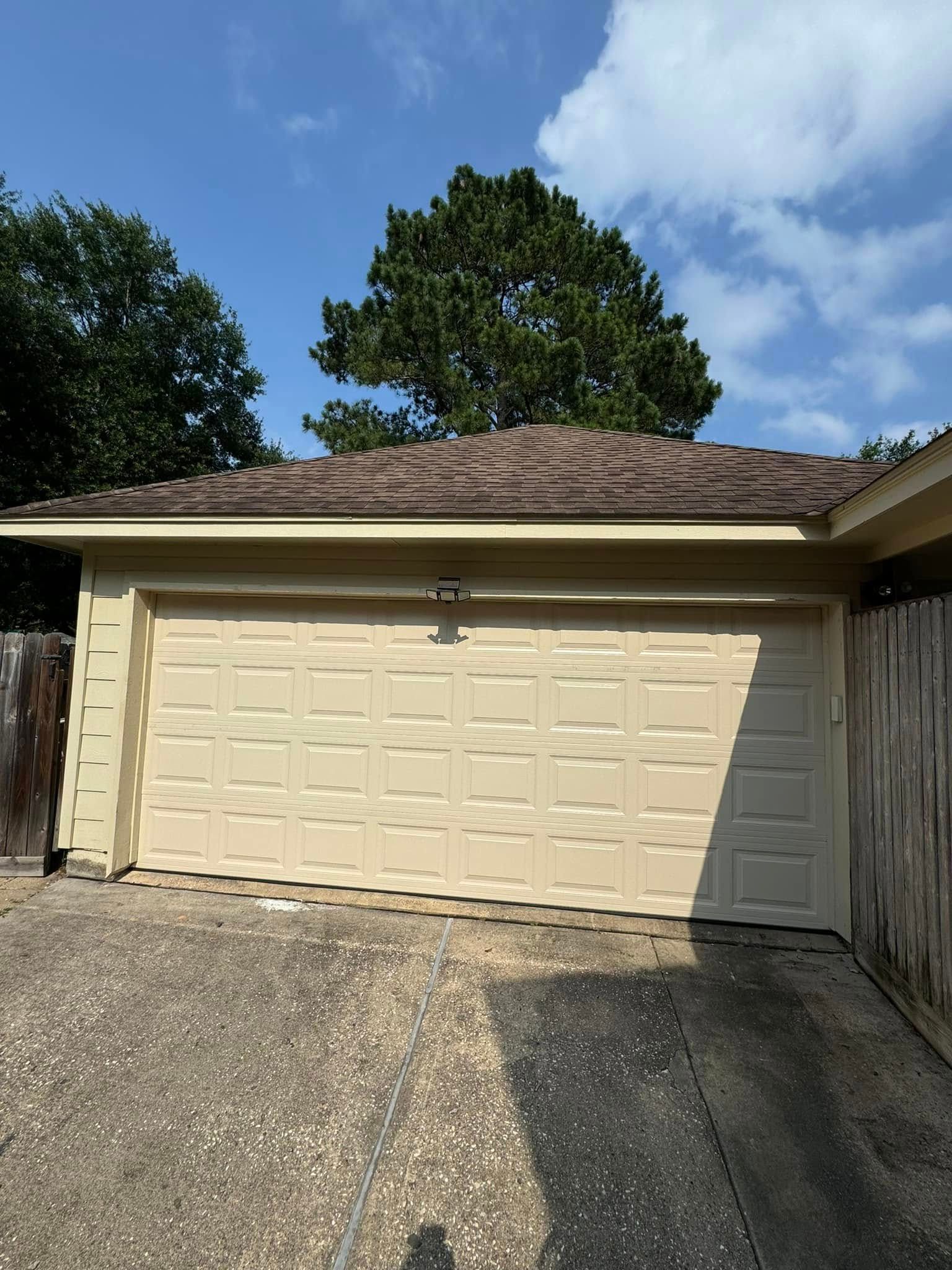 A beige two-car garage with a brown tile roof under a blue sky, viewed from a gravel driveway.