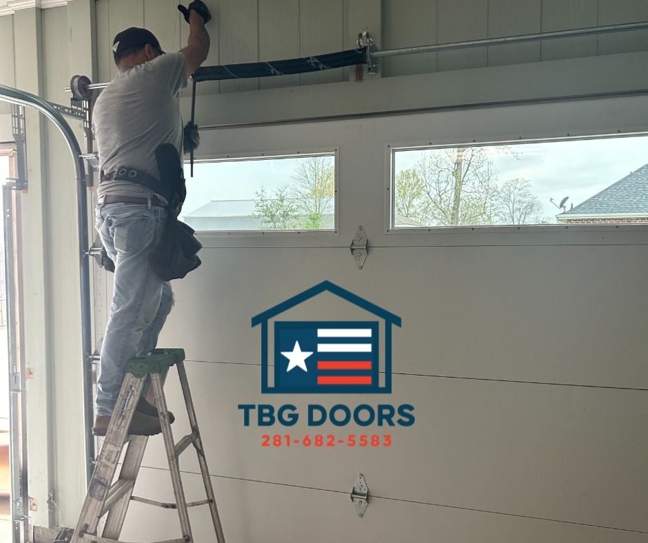 A technician stands on a stepladder while repairing a garage door. A