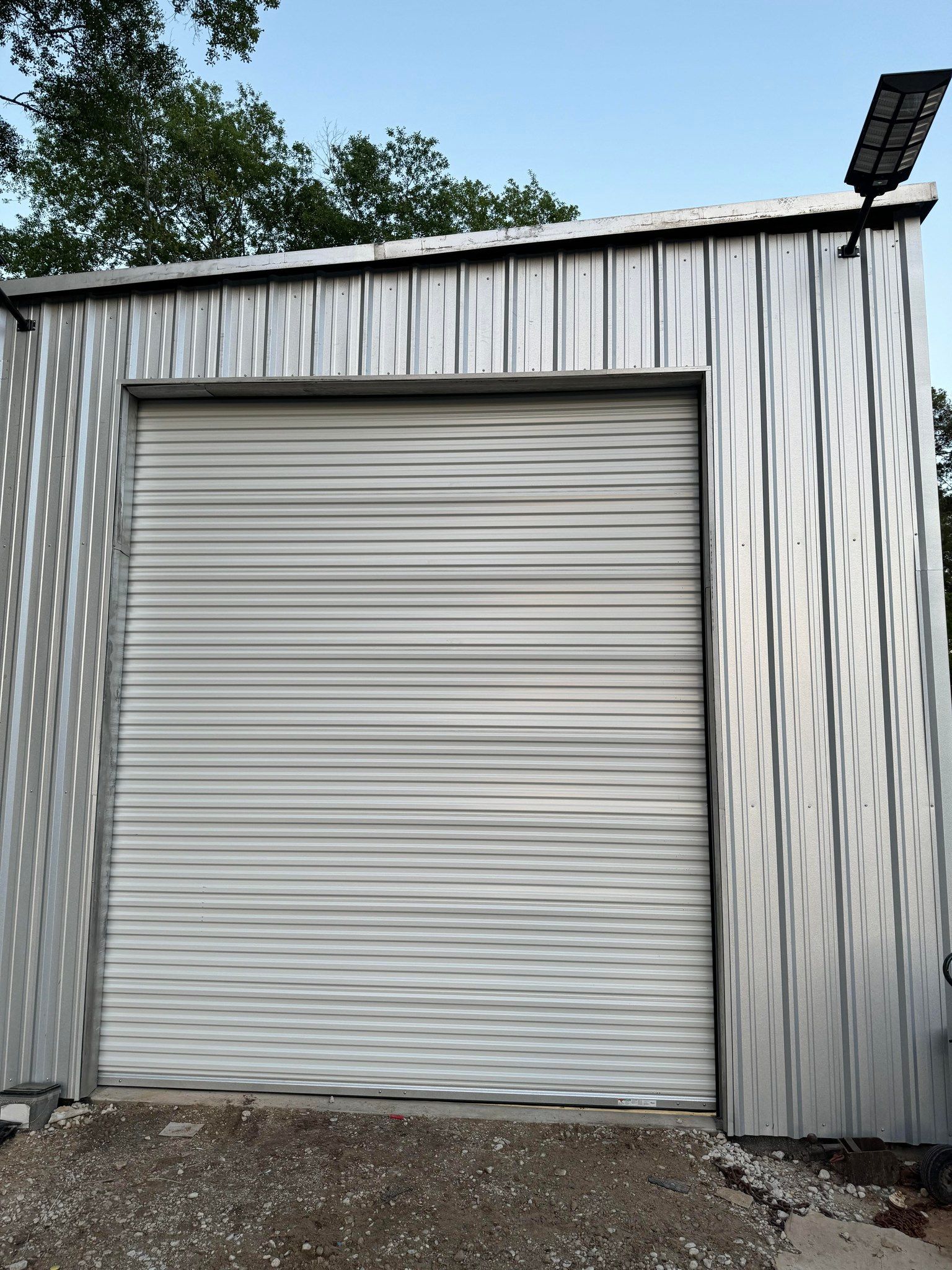 A metal garage structure with a closed rolling door, viewed from the front under a blue sky.