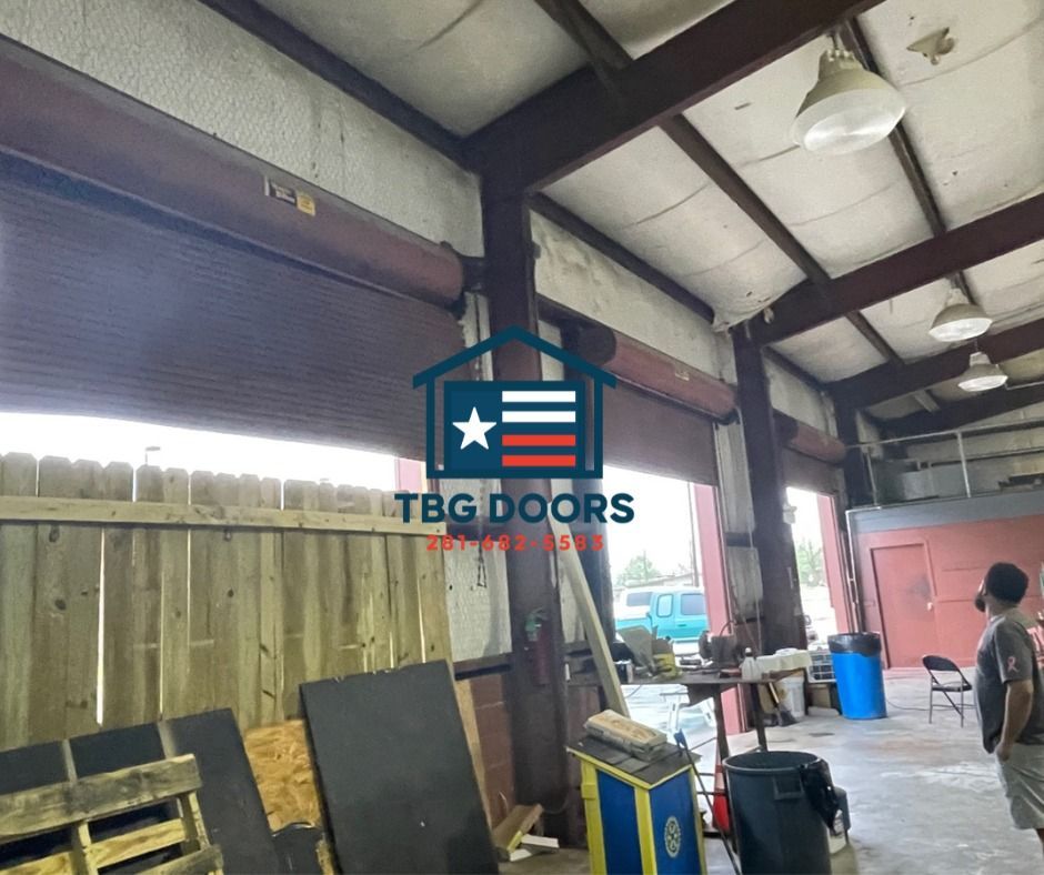 Interior view of a warehouse with roll-up doors, metal structural beams, and a person standing near work equipment.