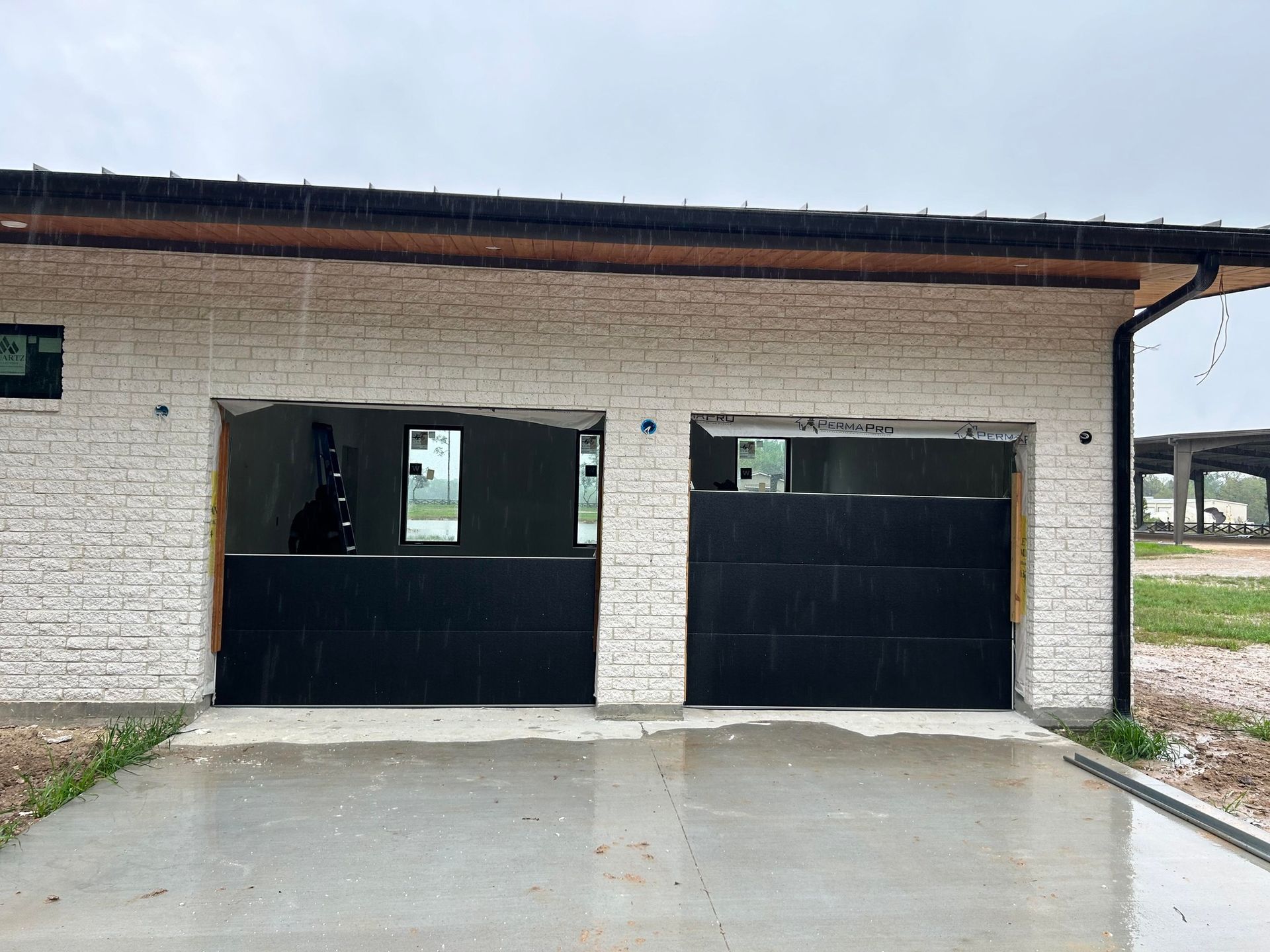 A building exterior with white stone walls and two garage openings partially covered by black horizontal panels.