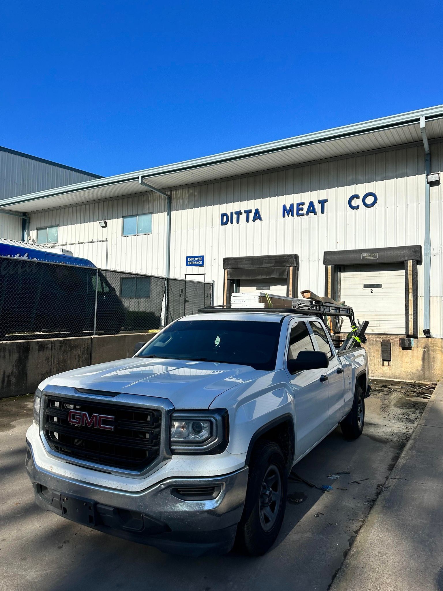 A white GMC pickup truck parked in front of a metal warehouse building labeled