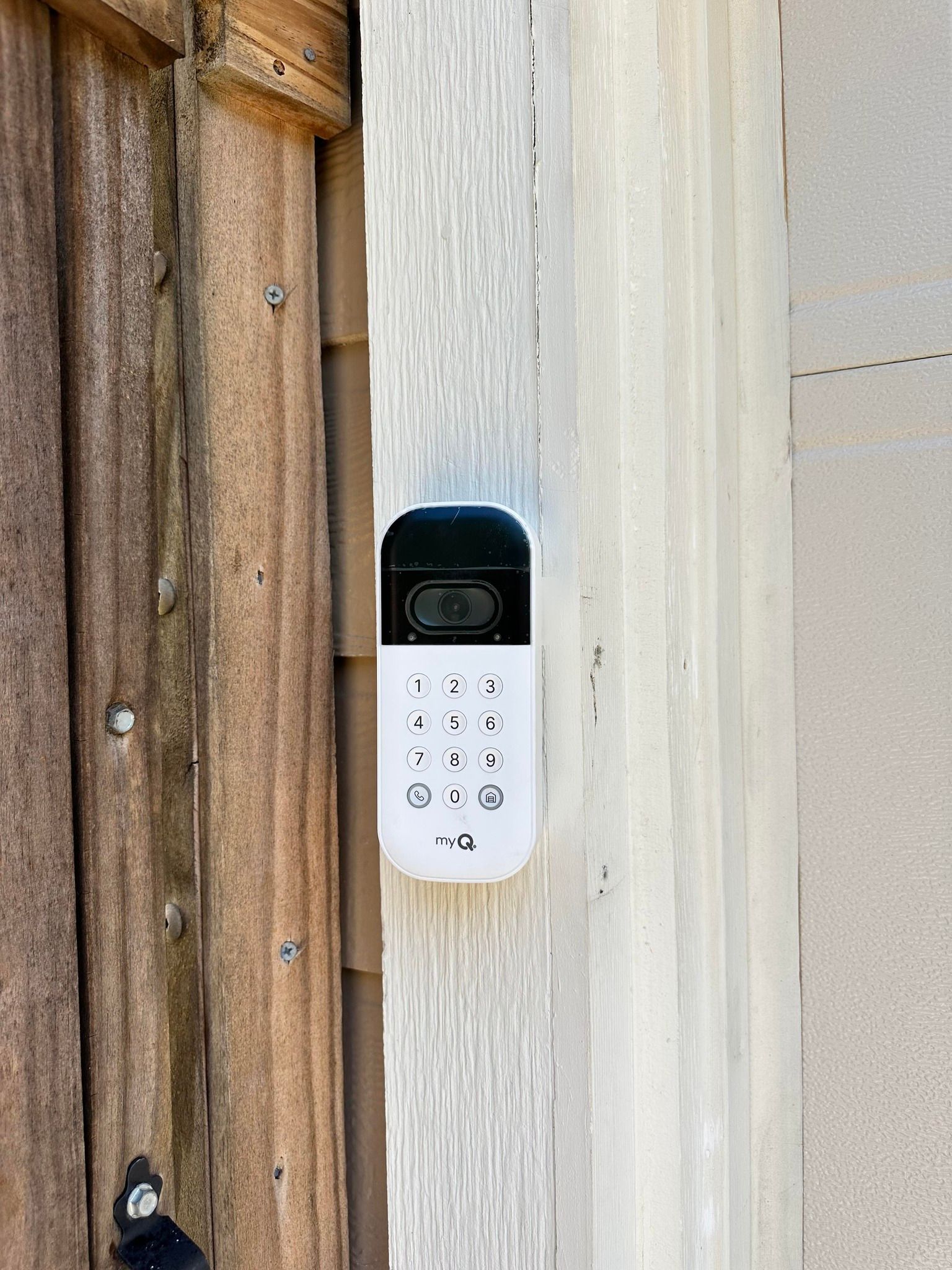 A white digital keypad security lock mounted on a white door frame next to a brown wooden door.