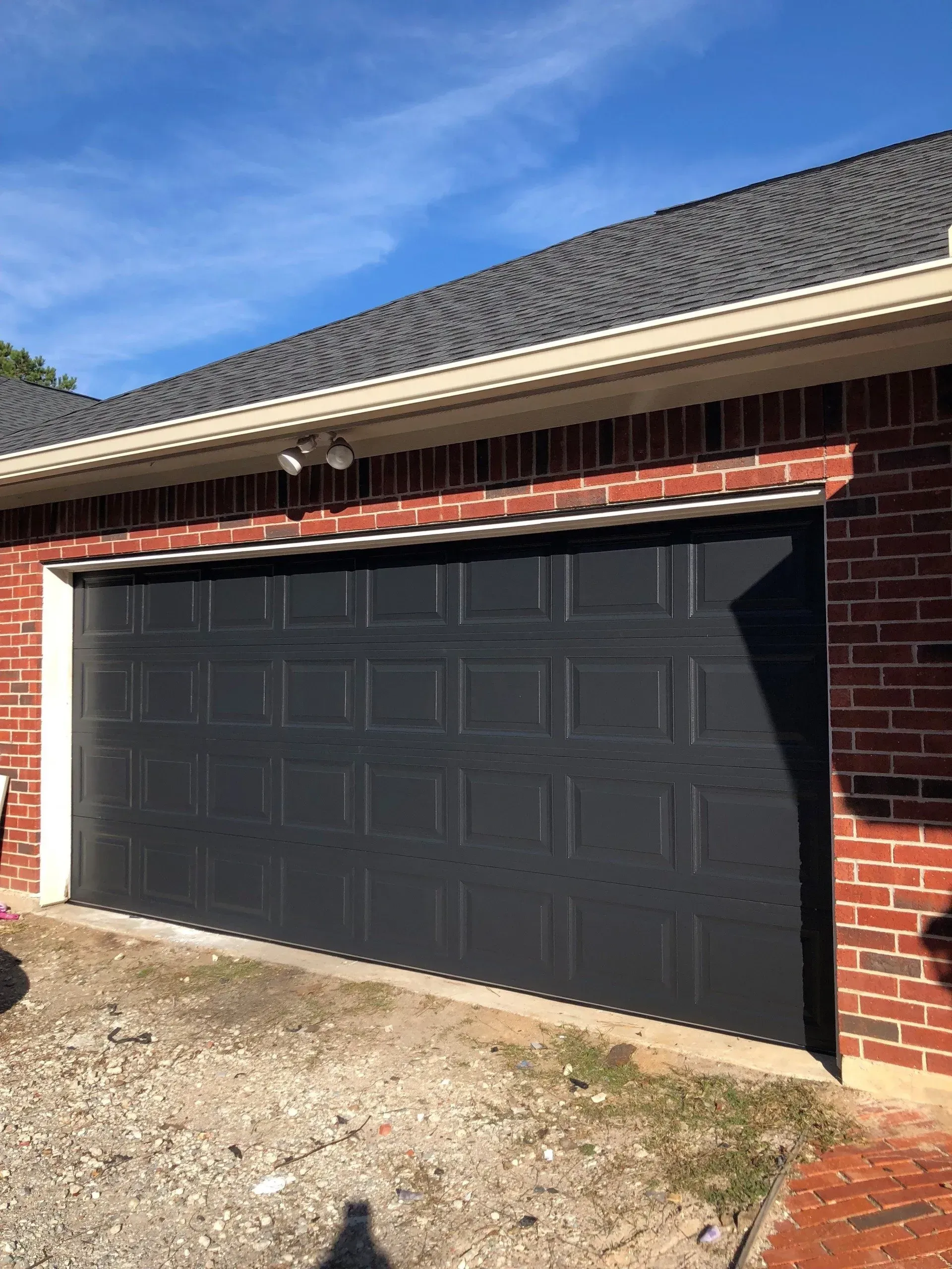 A black garage door with a grid panel design on a red brick house under a blue sky.