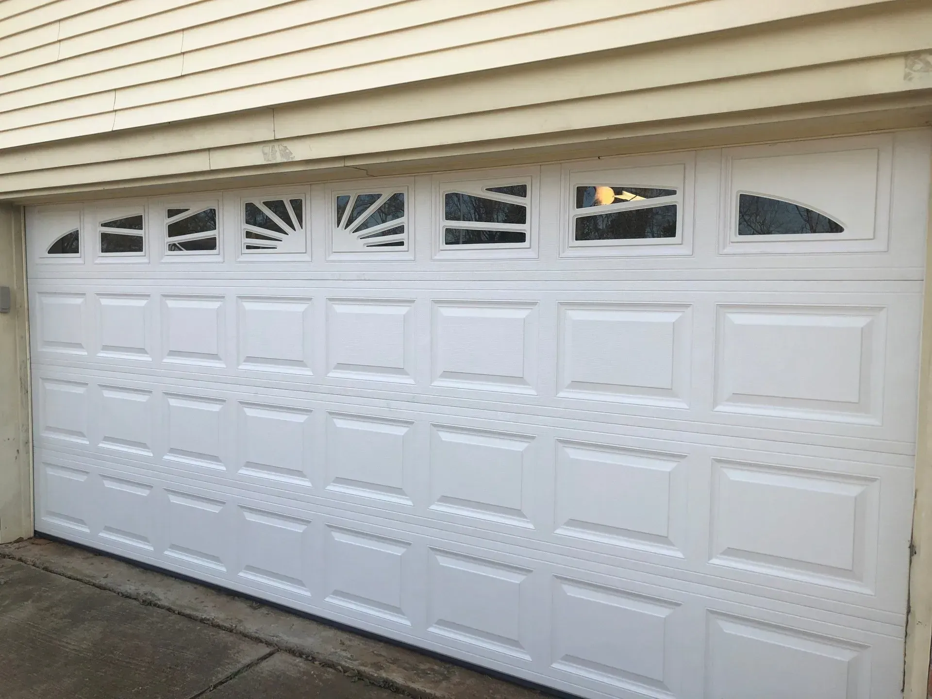 A white residential garage door with a sunburst window design in the top row and rectangular panel molding.