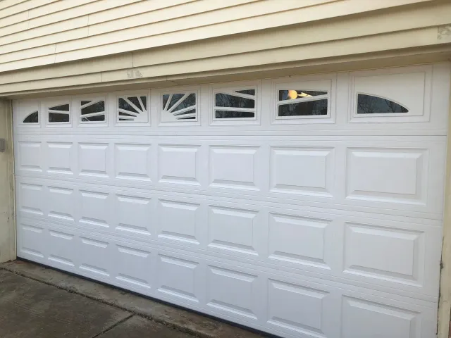 A white residential garage door with a sunburst window design in the top row and rectangular panel molding.
