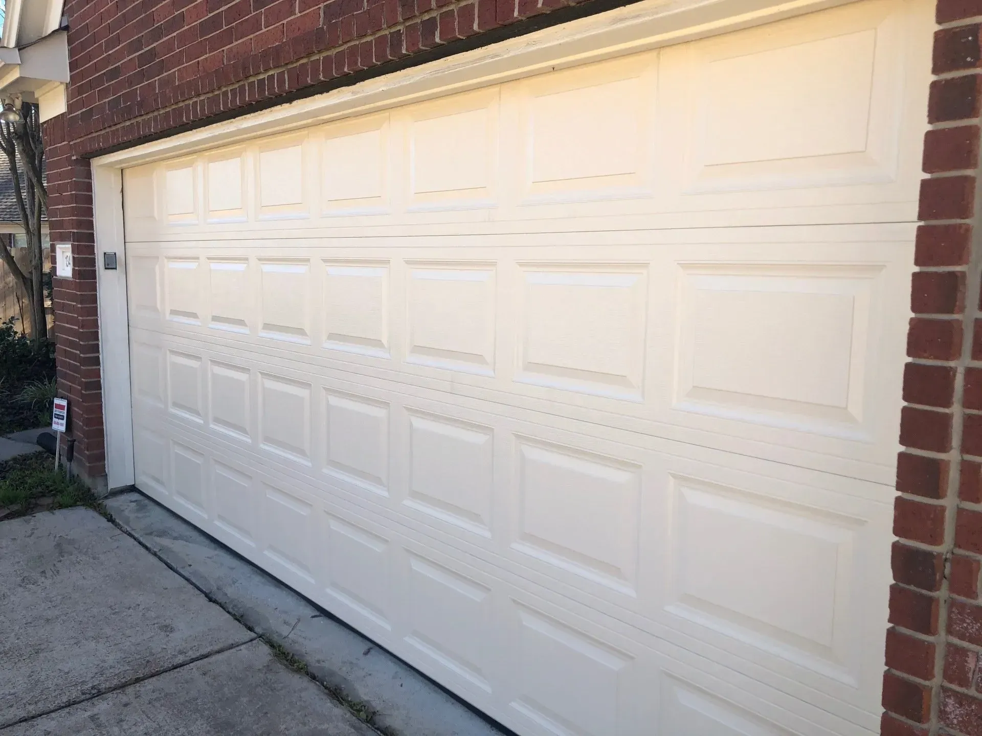 A white, four-panel residential garage door framed by red brick exterior walls.