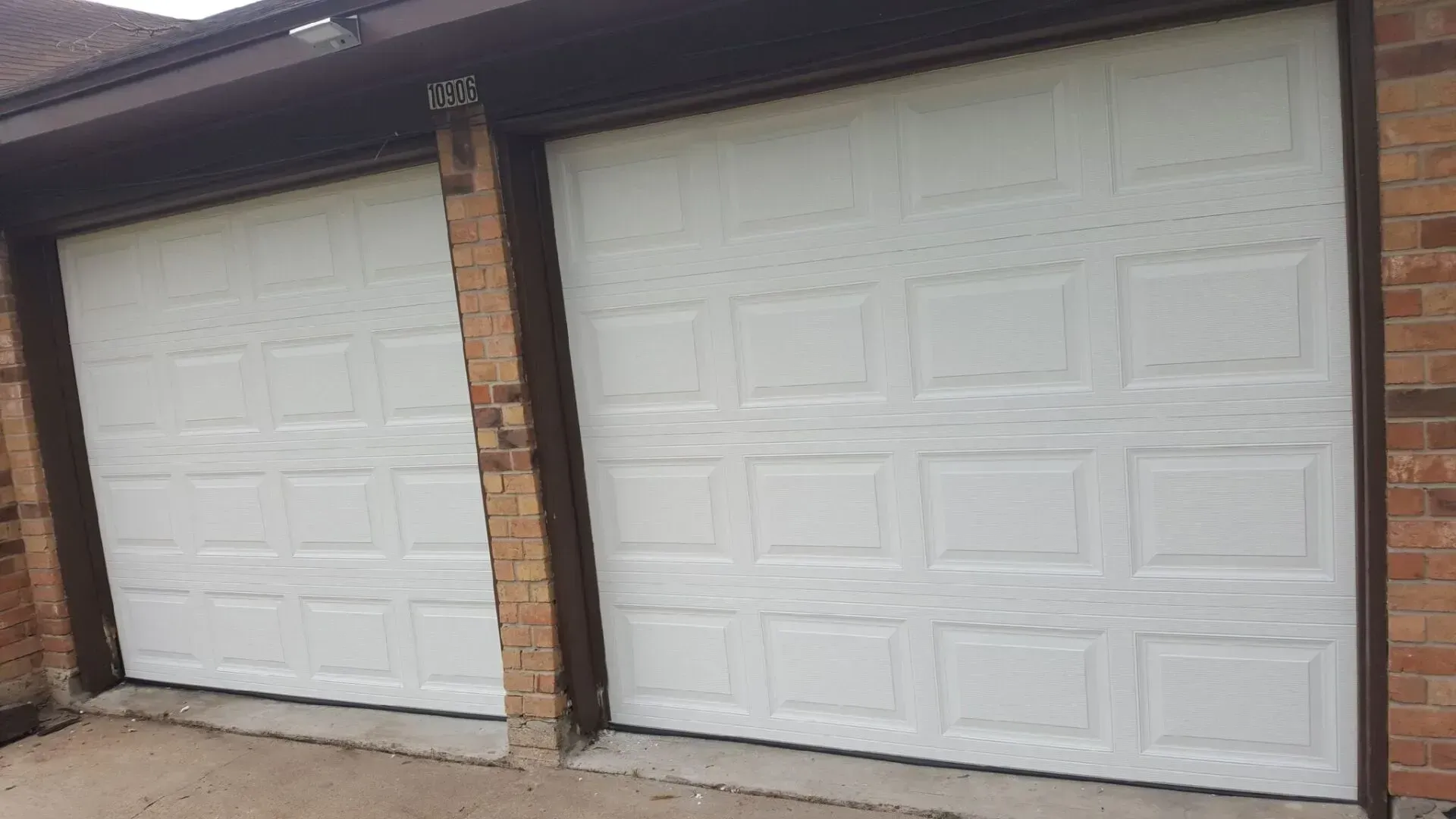 Two white, rectangular garage doors with a raised panel design, installed side-by-side in a brick home exterior.
