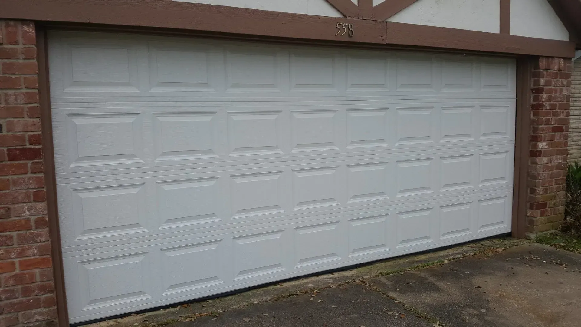 A white, multi-panel residential garage door with decorative textured middle panels, framed by brick walls.