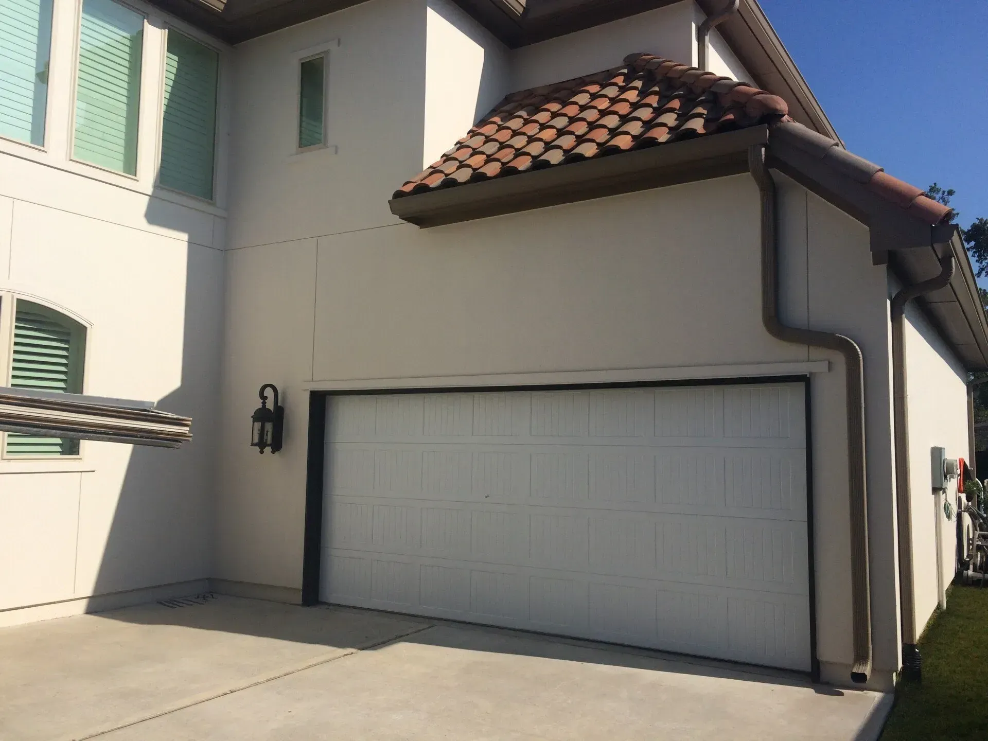 A white garage door with a tiled roof overhang on the exterior of a tan residential home.