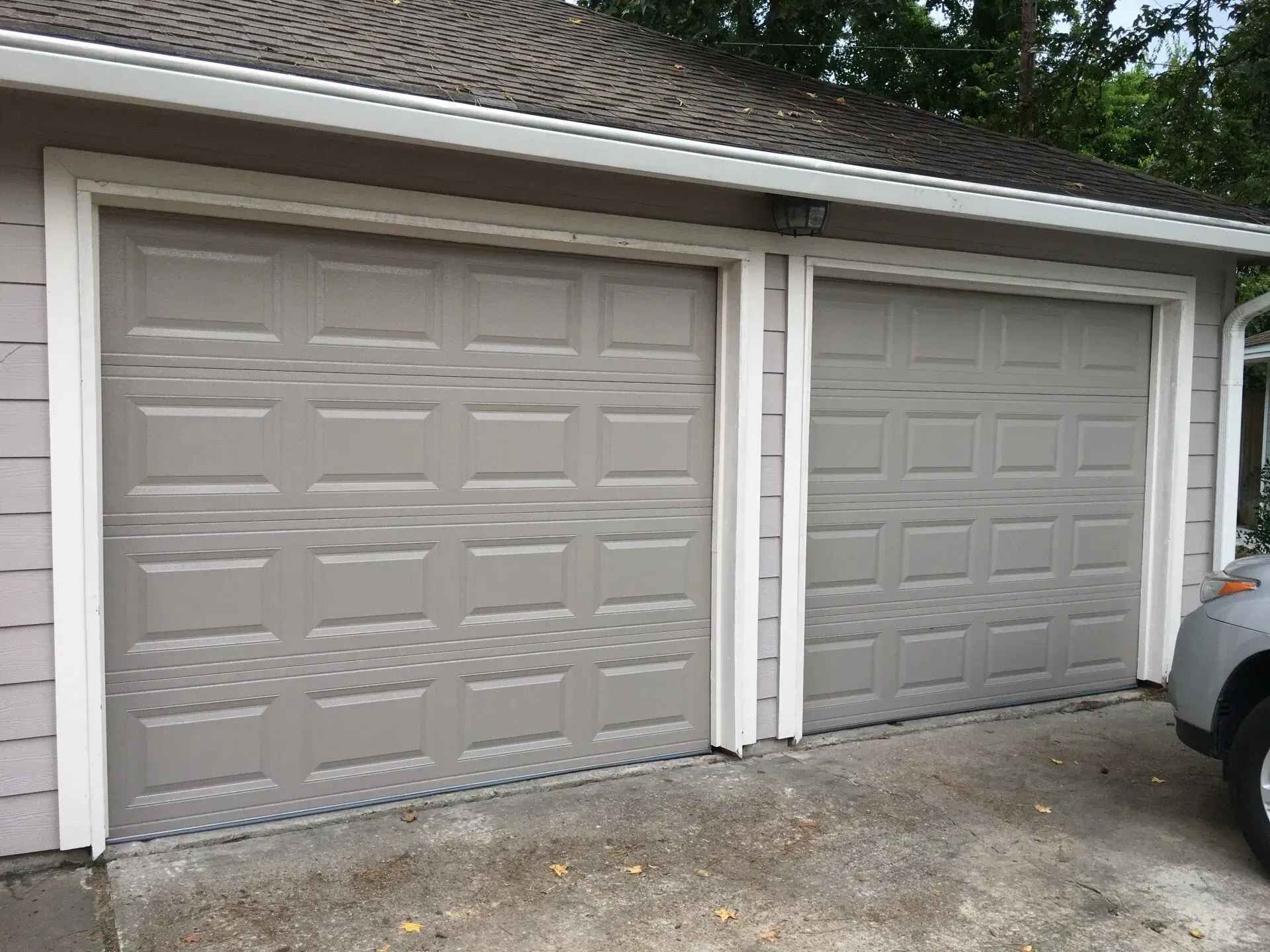 Two beige, paneled garage doors attached to a house, with part of a car visible on the right.
