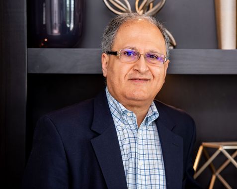 Man with glasses in blue blazer and shirt smiles in an office setting.