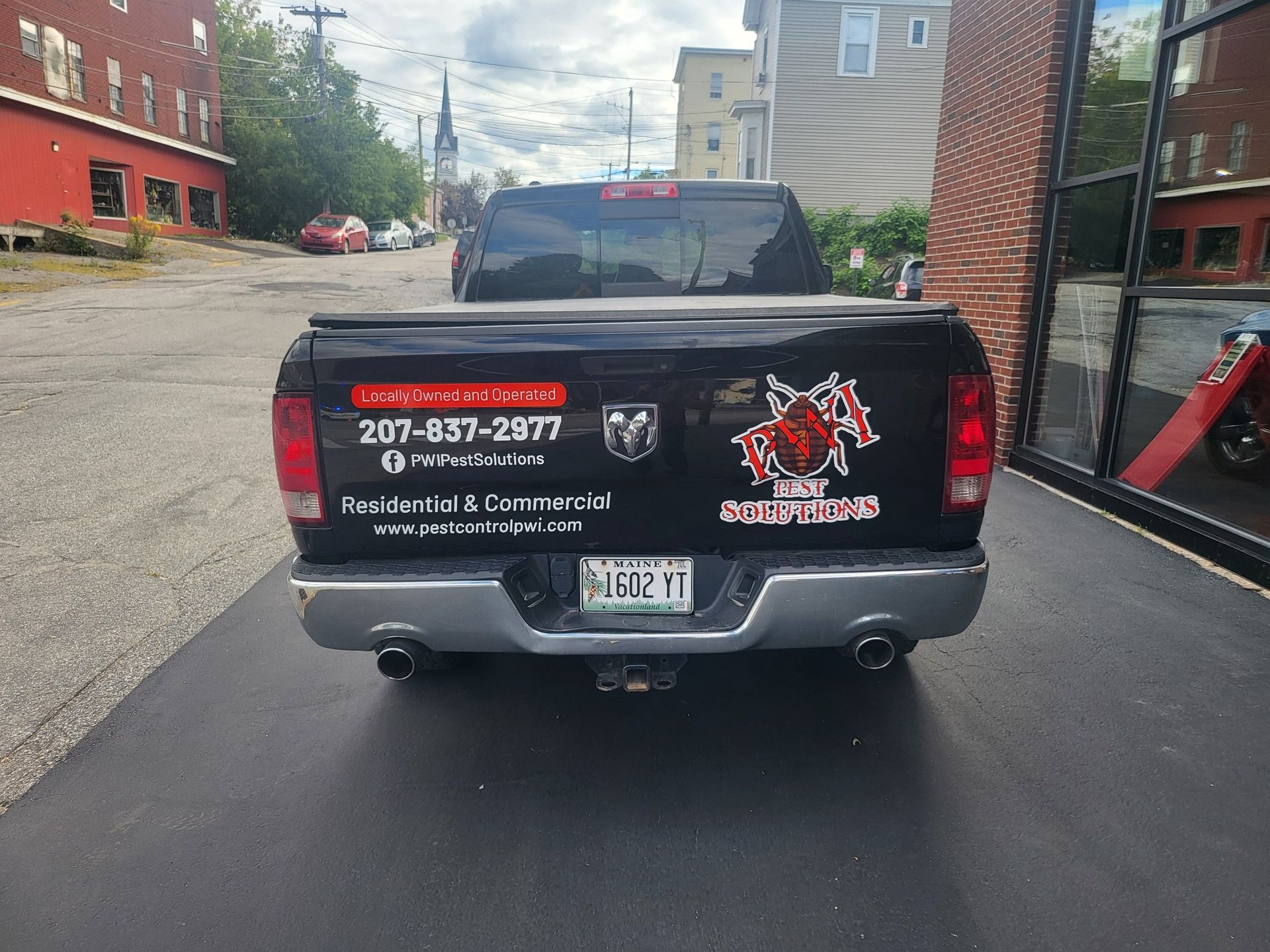 Pickup truck with business decals and phone number parked in a narrow alley.