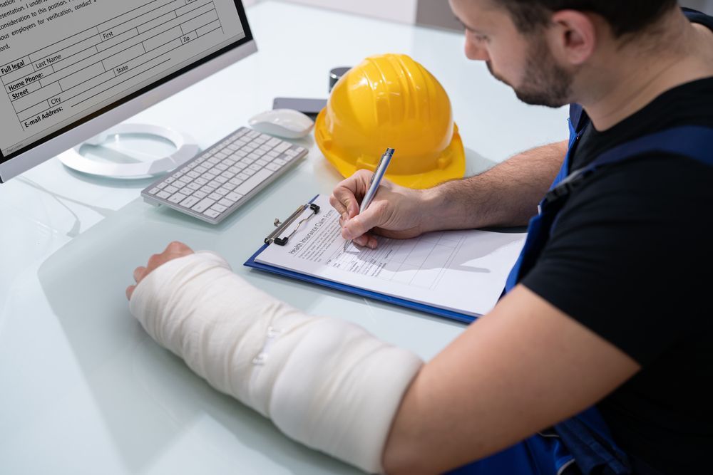 A man with a cast on his arm is sitting at a desk writing on a clipboard.