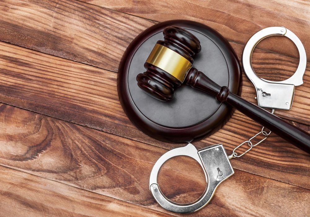 A judge 's gavel and handcuffs are on a wooden table.