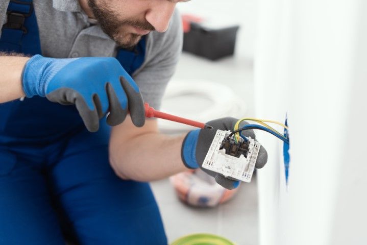 Electrician in blue gloves wiring an outlet box on a white wall