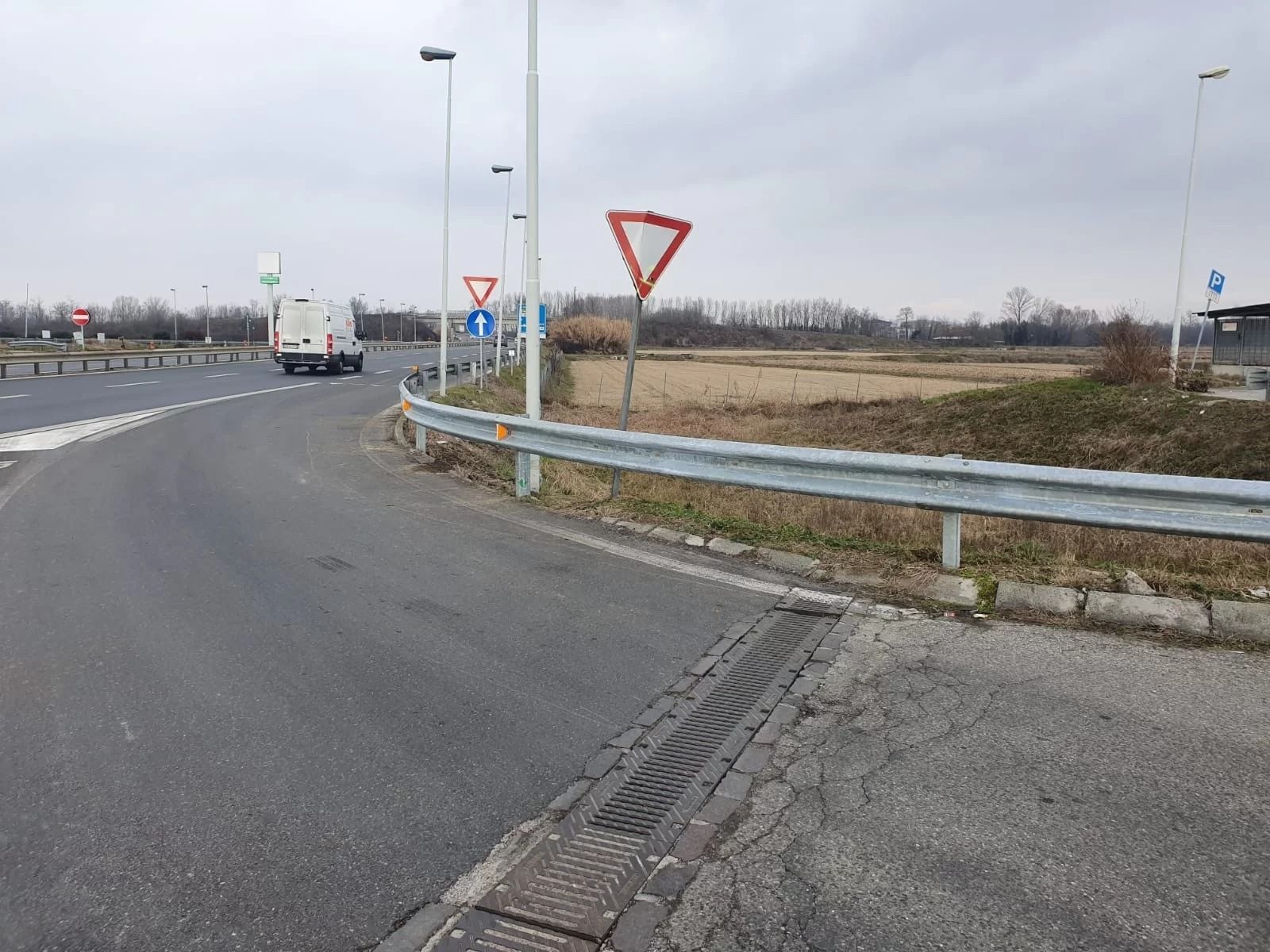 Una vista da una strada di accesso su un incrocio con segnali di precedenza e un furgone bianco che percorre la strada principale.