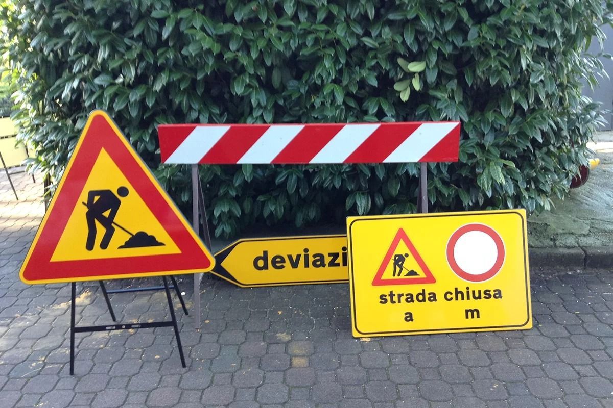 Segnaletica stradale relativa ai lavori in corso, tra cui un segnale triangolare di pericolo, una barriera a strisce, un segnale giallo di deviazione e un segnale di strada chiusa.