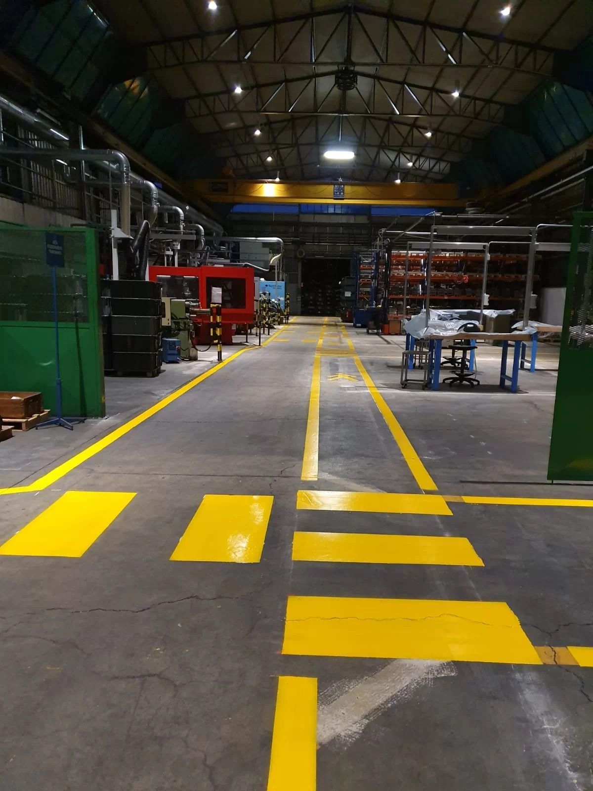 Il pavimento di una fabbrica è delimitato da segnaletica orizzontale gialla, con linee e strisce pedonali che conducono all'interno dello stabilimento.