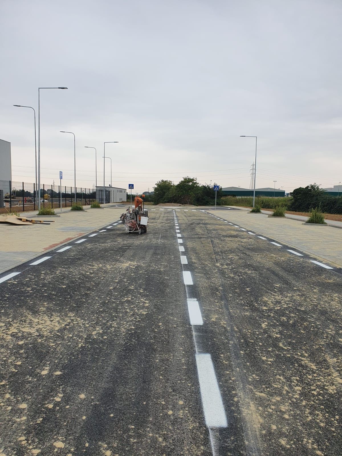 Una persona è seduta su un piccolo scooter per disabili al centro di una strada asfaltata appena pavimentata, con corsie bianche appena dipinte.