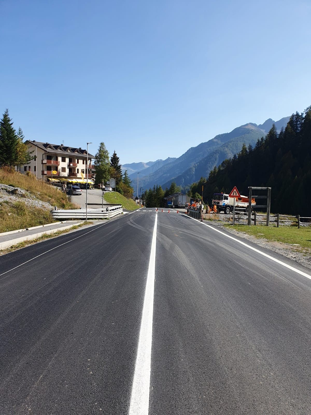 Una strada dritta, appena asfaltata, con una linea bianca al centro, che si snoda verso le montagne sotto un cielo azzurro e limpido.