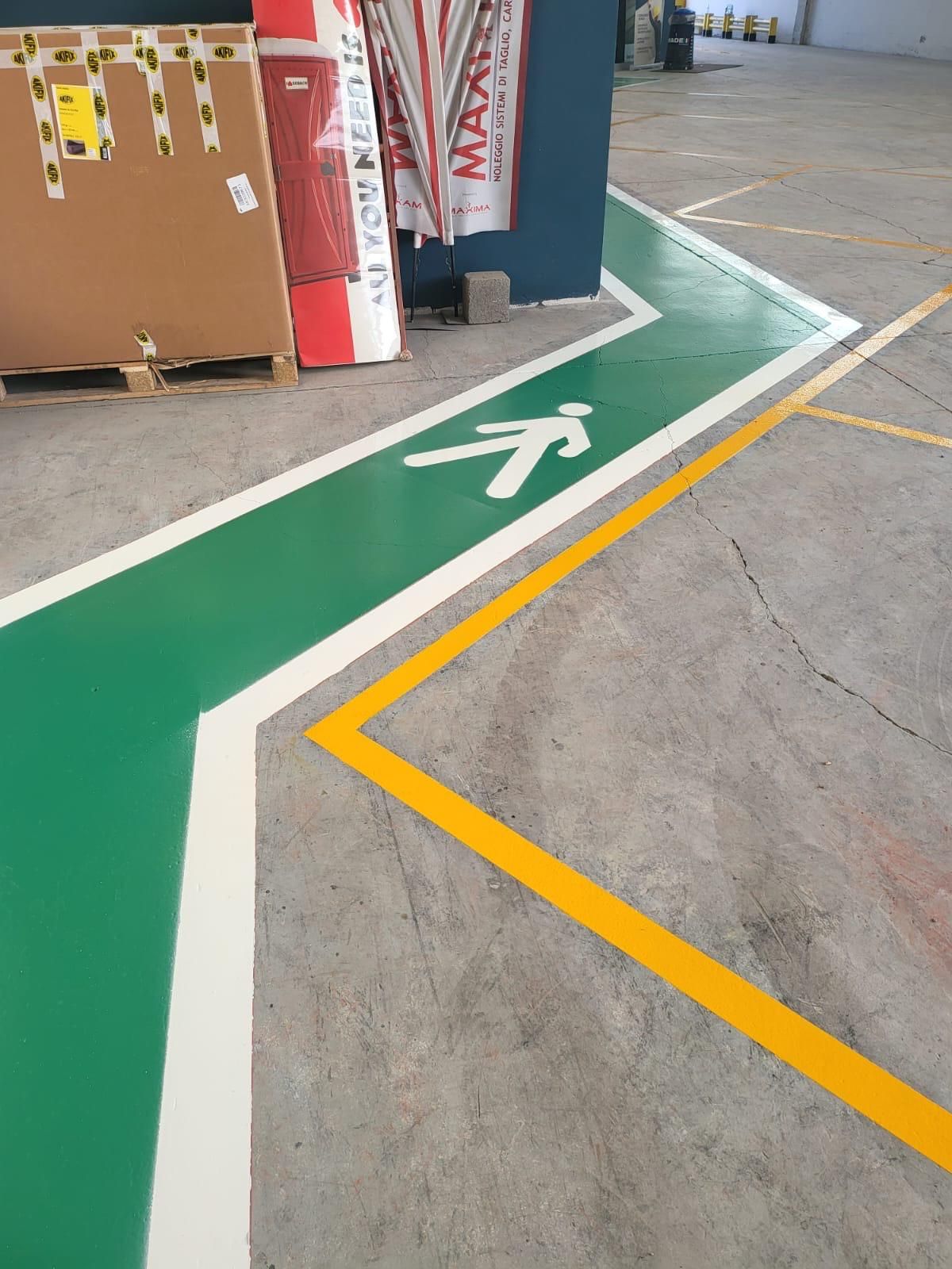 Un percorso pedonale verde con l'icona di una figura umana che cammina dipinta su un pavimento di cemento accanto a una linea gialla.