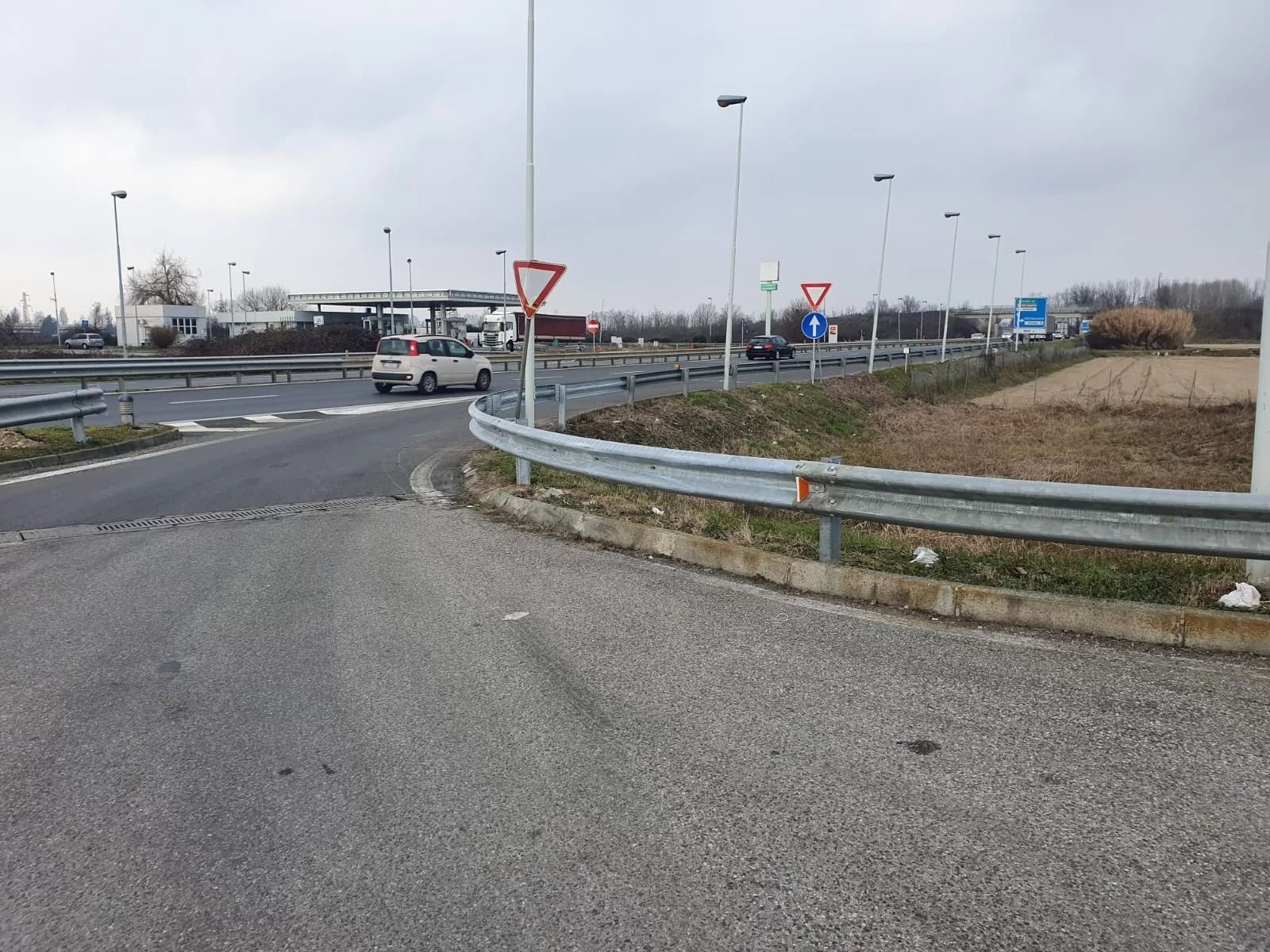Un incrocio con un'auto bianca che si avvicina a un segnale di precedenza vicino a una stazione di servizio sotto un cielo nuvoloso.
