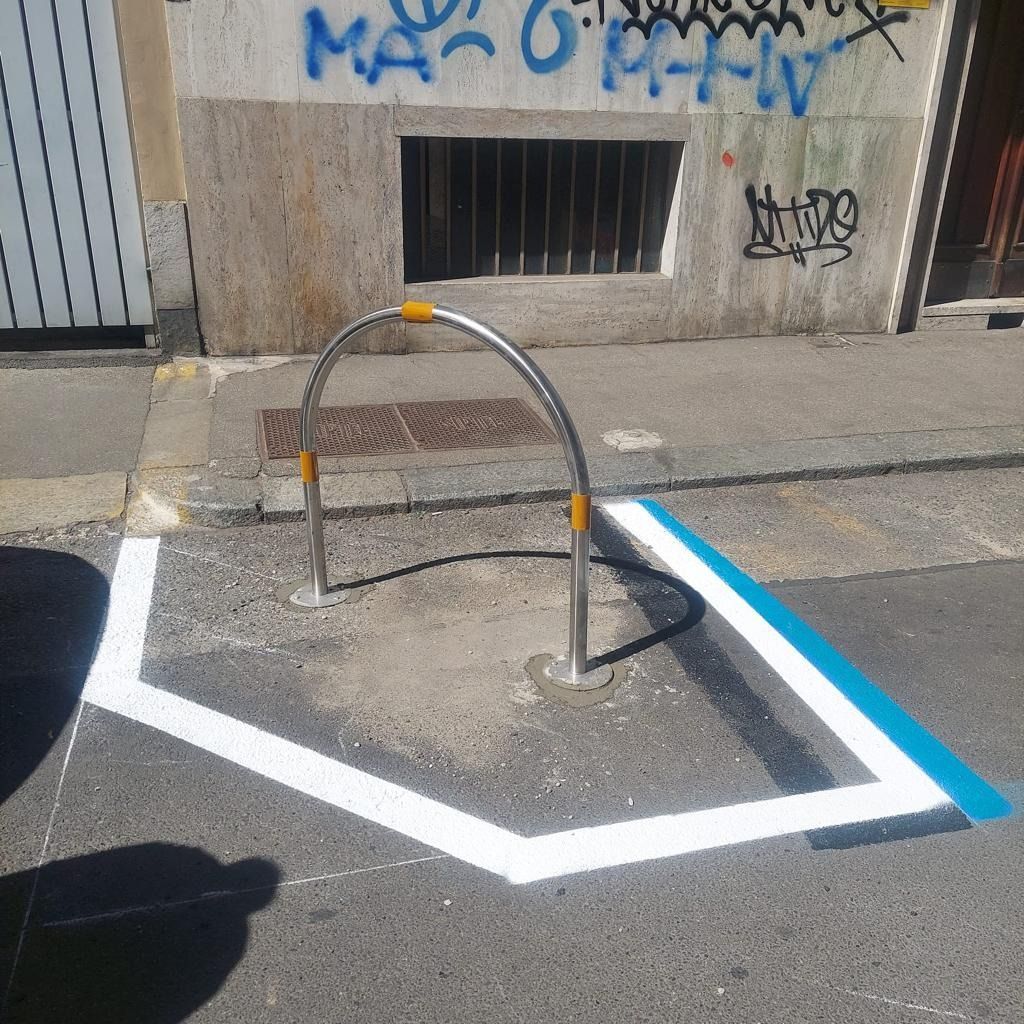 Una rastrelliera metallica per biciclette su un marciapiede, segnalata da linee bianche e blu dipinte sul terreno.