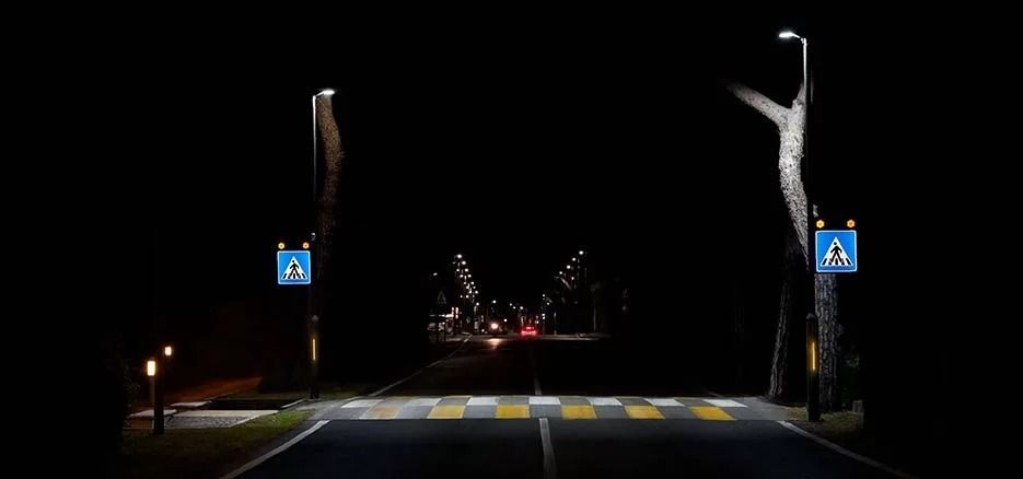 Un attraversamento pedonale ben illuminato di notte, con strisce gialle e bianche e segnali di attraversamento blu su entrambi i lati.