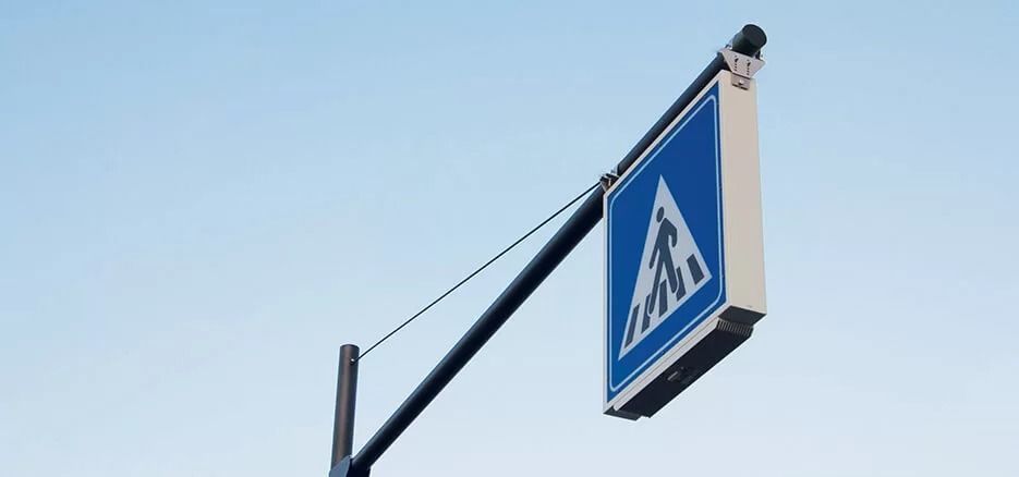 Un cartello pedonale quadrato blu e bianco, fissato a un palo di metallo, stagliarsi contro un cielo limpido.