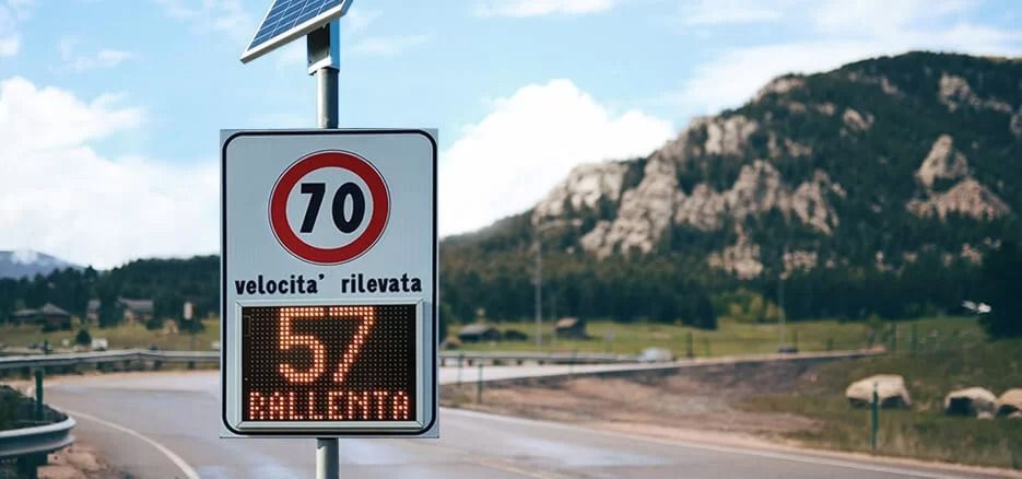 Un cartello stradale con rilevatore di velocità radar indica una velocità di 57 km/h con la scritta in italiano 