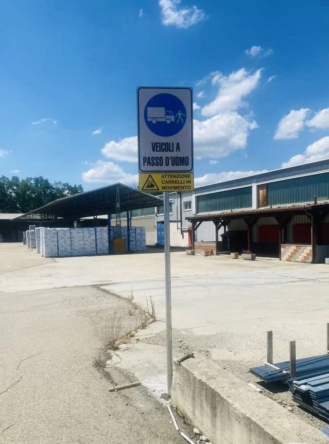 Un palo di metallo sorregge un segnale circolare blu di obbligo con il simbolo di un camion e di un pedone, con la scritta 