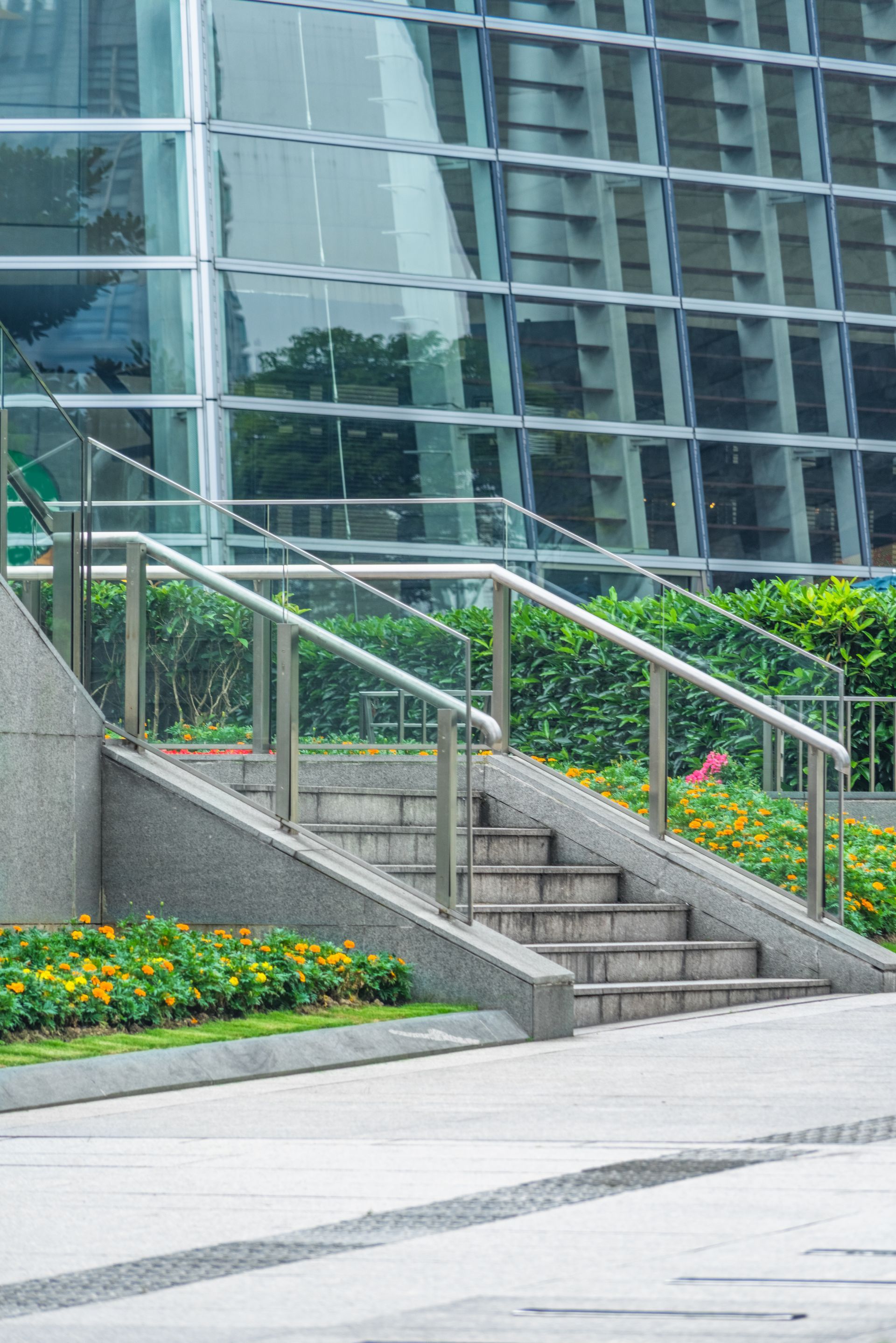 Staircase with metal railings next to a glass-paneled building and flower beds.
