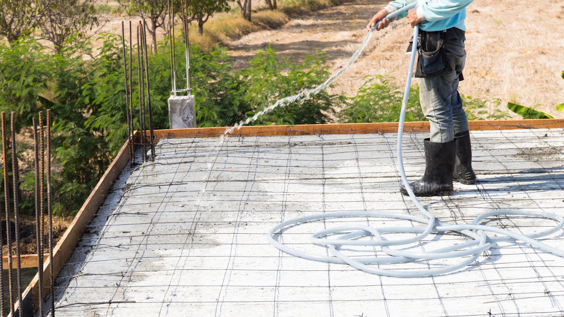 Construction worker in Peterborough spraying water on a concrete slab that is being installed in a backyard.