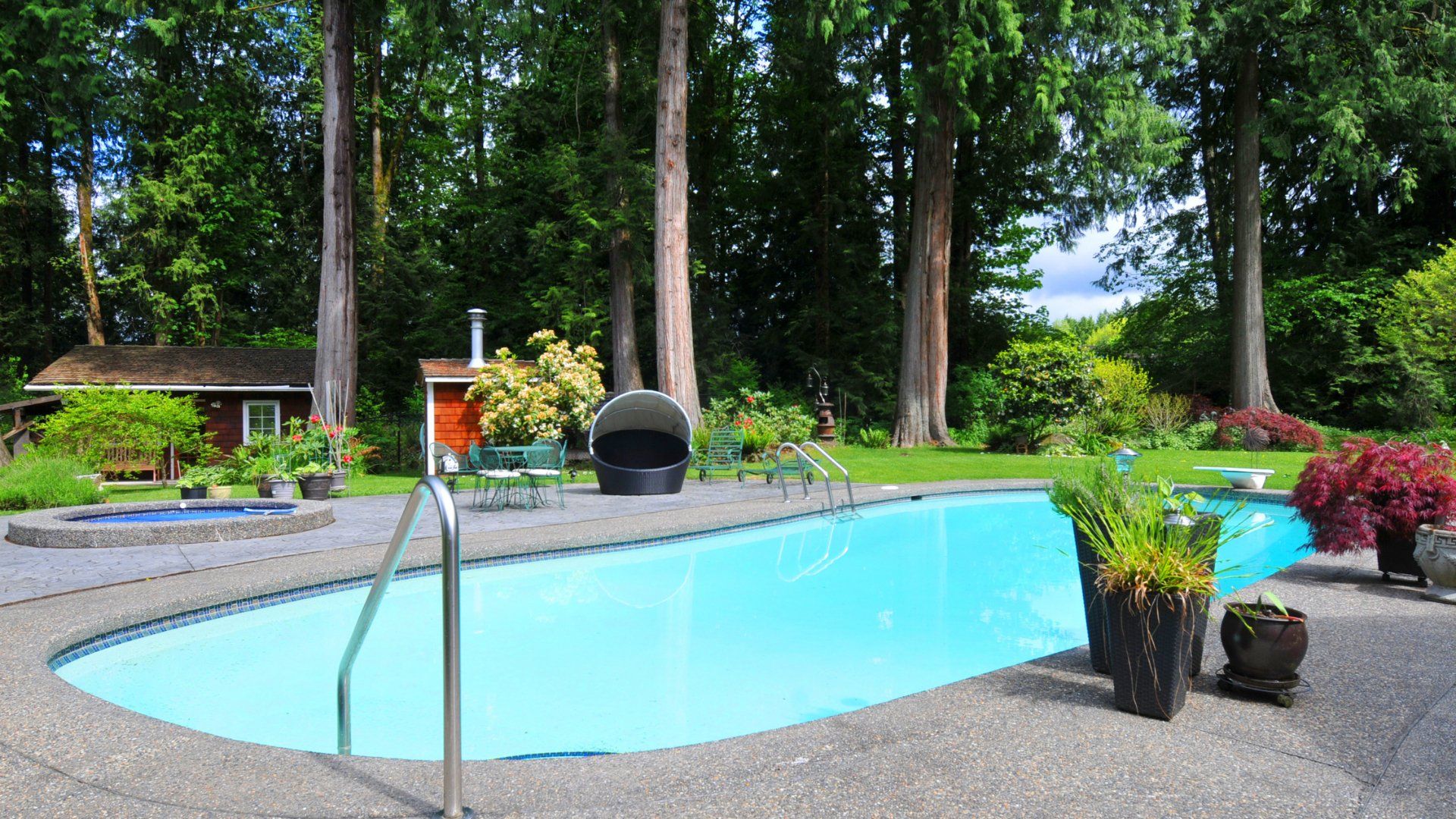 Large backyard featuring a pool, large trees, jacuzzi, pool house, and a concrete pool deck.