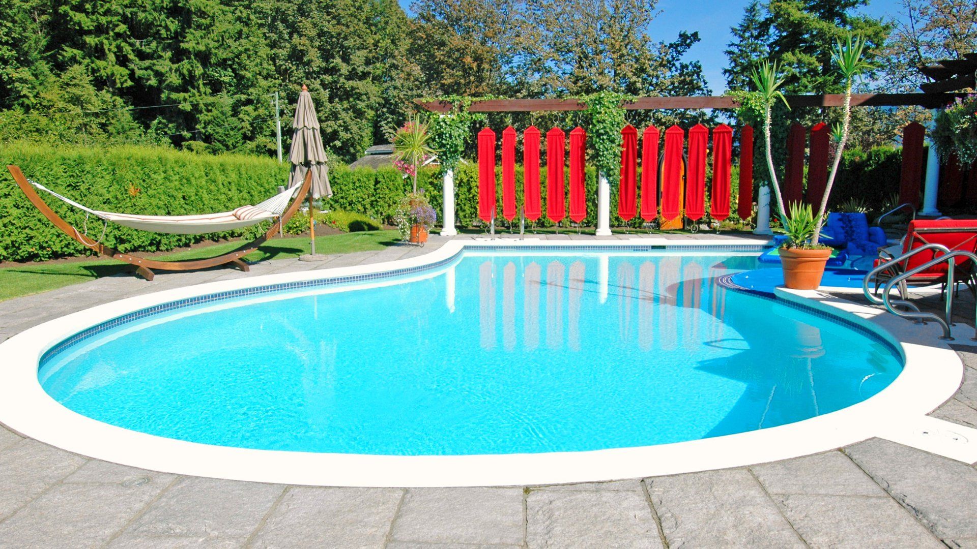Backyard pool with a stamped concrete pool deck.  The backyard is lined with cedar hedges.  There is a hammock and some modern looking decorations.